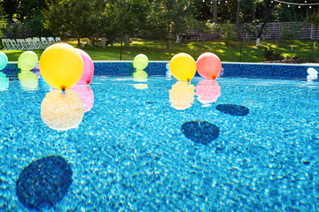 Swimming pool with colorful balloons on blue water outdoor, copy space. Poolside party in garden. Air balloons on water. Decorations for wedding ceremony in the pool