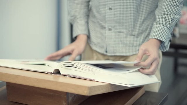 Male hand opening recommended book page on book stand. Young university student man doing self-study for educational research in college library. Education lifestyle concept. 4K video