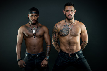 Fototapeta na wymiar Guys sportsmen with sexy muscular torsos. Athletes on confident faces with nude muscular chests. Sexy body concept. Machos with muscular tattooed torsos look attractive, dark background