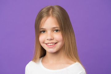 Fototapeta premium Girl on smiling face with long hair wears white shirt, violet background. Girl likes to look cute, stylish and fashionable. Kid girl with long hair looks adorable. Hairstyle and hair care concept