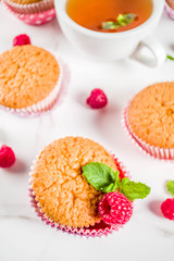 Sweet summer dessert, homemade baked muffin with raspberry jam, served with tea, fresh raspberries and mint. On a white marble table, copy space