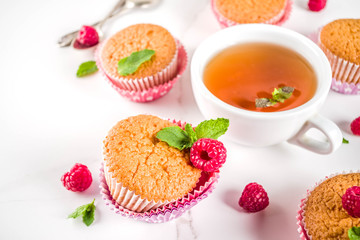 Sweet summer dessert, homemade baked muffin with raspberry jam, served with tea, fresh raspberries and mint. On a white marble table, copy space