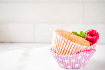 Sweet summer dessert, homemade baked muffin with raspberry jam, served with tea, fresh raspberries and mint. On a white marble table, copy space