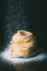 close up image of flour falling on raw tagliatelle pasta on black background