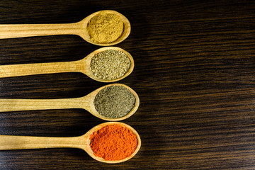 Spoons with the different spices on dark wooden table. Top view