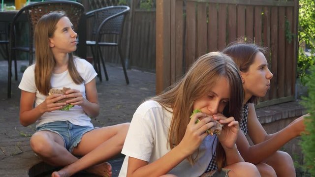 Triple sisters twins teen girls sitting on backyard porch terrace eating sandwiches