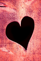 Hole in the shape of the heart in a pink wood panel