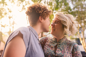 Young lesbian couple laughing together other on a sunny street - obrazy, fototapety, plakaty