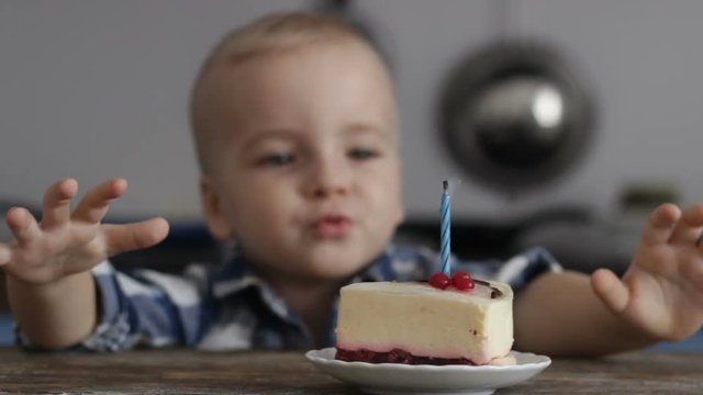 Blonde, happy, smiling boy blowing out a candle on cake. One-year celebration
