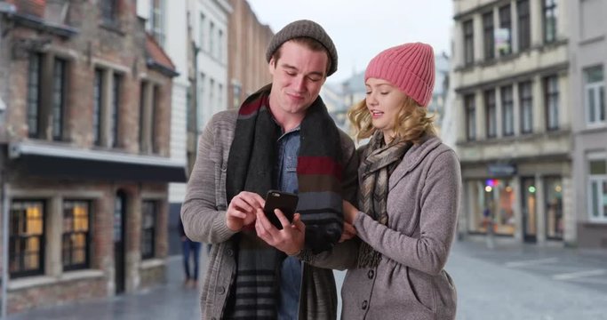 Attractive Caucasian male and female exploring Belgian streets, walking arm in arm, Tourists using smartphone for directions, 4k