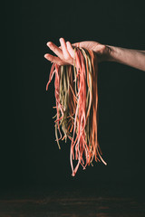 cropped image of man holding raw colorful tagliatelle on hand over table on black background