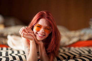 pretty young woman with red hair and sunglasses lies relaxed and laughing on the couch, emotion...
