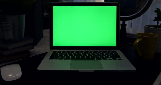 Laptop with green screen. Dark office. Dolly in . Perfect to put your own image or video.Green screen of technology being used. Chroma Key laptop