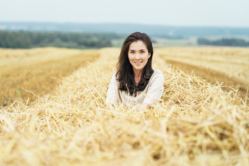 Young smiling white farmer woman is sitting in freshly cutted hay in the field. Rural lifestyle concept