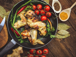 fried chicken wings in a frying pan. tomatoes and spices. wooden background