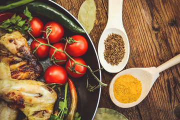 fried chicken wings in a frying pan. tomatoes and spices. wooden background