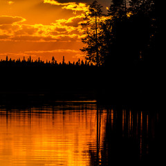 Fantastic sunset on the lake, dark pine forest reflecting in the calm water