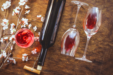 glasses with red wine, a bottle, a flowering branch. wooden background.
