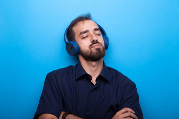 Young man listening to music through headphones on blue background 