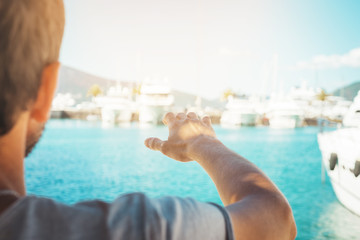 Young man at beatiful port marina with raised hand. Luxury lifestyle reaching concept...Close up. Selective focus, copy space.