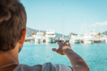 Young man at beatiful port marina with raised hand. Luxury lifestyle reaching concept...Close up. Selective focus, copy space.