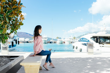 Young woman sitting in the beautiful marina surrounded by luxurious yachts