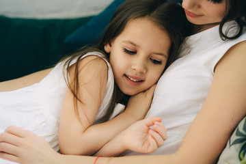 Close up of mother and daughter cuddle on the green sofa. Tender moments of parenting.