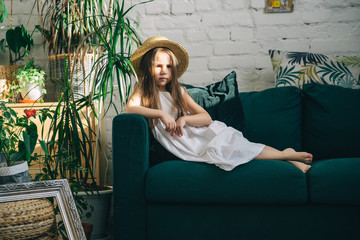 Cute little girl is lying on the green sofa\couch indoor plants around. Summer vacation begins.