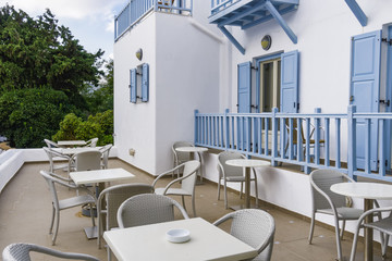 Mykonos, Greece traditional apartment house external view. Day view of hotel entrance atrium with white walls and blue balconies with dining chairs and tables next to public courtyard.