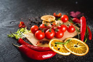 Fresh cherry tomatoes and spices on black background. Top view. Copy space
