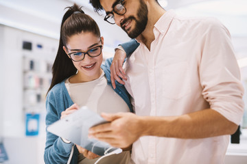 Cute young couple is checking out a test tablet in a bright tech store.