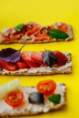 Healthy snack with crispbread, cream cheese, strawberry, grapefruit, tomato and cucumber on a yellow background