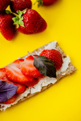 Snack with crispbread, cream cheese, fresh strawberry and basil on a yellow background