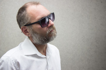 Obraz premium A man in a shirt with a beard in glasses is standing by the wall