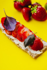 Snack with crispbread, cream cheese, fresh strawberry and basil on a yellow background
