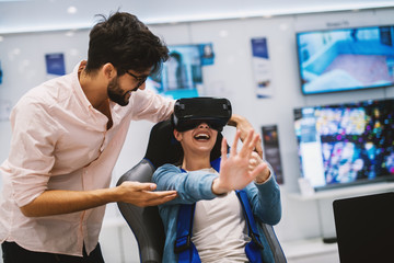 Young cheerful girl is using VR systems while a young handsome man is holding her.