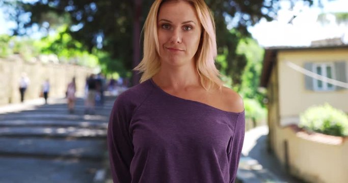 Nonchalant young white woman in purple shirt standing outside in Italian setting, Pretty young woman looking casually at camera outside while in Italy in the daytime, 4k