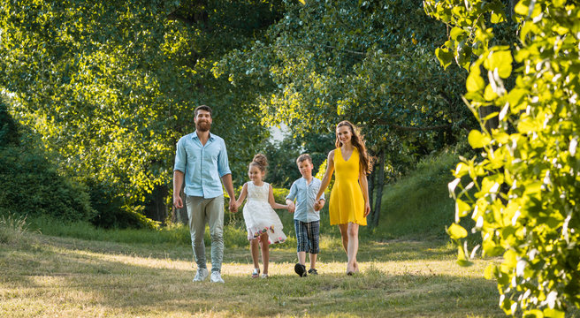 Full length view of a happy family with two children wearing casual summer clothes while holding hands during recreational walk in the park