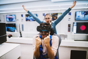 Young cheerful man is celebrating victory in a game while using VR and his girlfriend is celebrating with him.