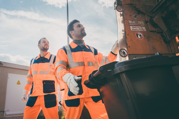Two garbagemen working together on emptying dustbins for trash removal