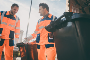 Garbage removal men working for a public utility emptying trash container