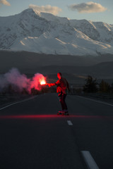 Teenage girl with red fire of counterfeit skateboarding on road  in mountains