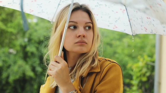 closeup portrait of beautiful woman with umbrella scared of the rain lightning strike then smiling and looking at camera with forest on blur background joyful mood fun joy falling raindrops day light