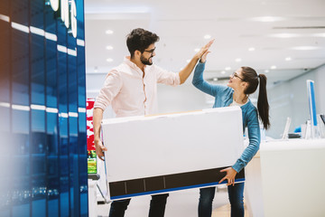 Young beautiful playful couple is celebrating buying a new TV by high-fiving.