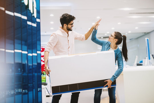 Young Beautiful Playful Couple Is Celebrating Buying A New TV By High-fiving.