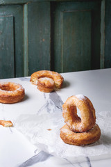 Homemade puff pastry deep fried donuts or cronuts with sugar standing on crumpled paper over white marble kitchen table.