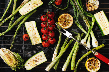 Grilled vegetables green asparagus, garlic, lemon, spring onion, zucchini, cherry tomatoes, salad on bbq grill rack over charcoal. Top view. Barbecue concept