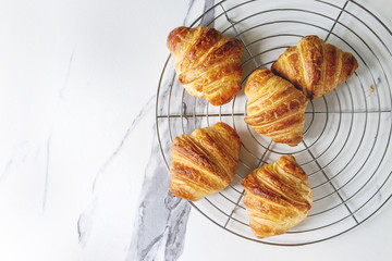 Homemade croissant on cooling rack over white marble background. Flat lay, space.