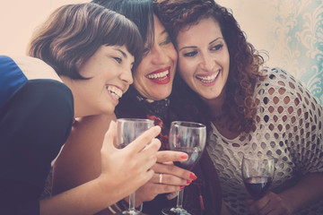 three happy and beautiful females friends have fun together at home drinking some red wine and enjoying the leisure and tie friendship. relationship with friends concept in vintage colors