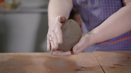 female hands are kneading and beating clay in art pottery workshop, shaping ball for making ceramic goods